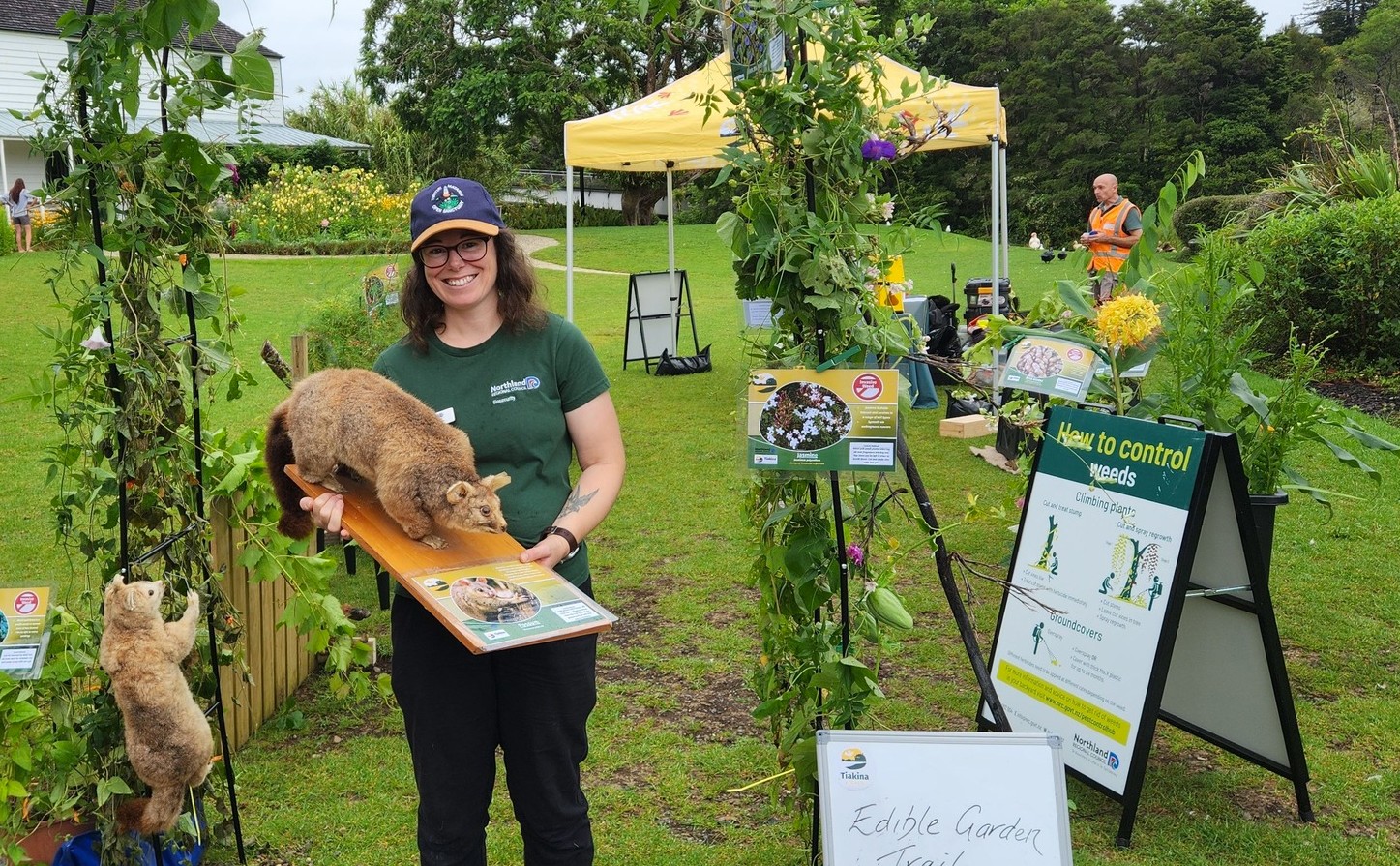 Emily holding a taxidermy possum in amongst a variety of pest plants on display to the community.